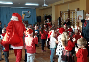 dzieci podczas tańca witają Mikołaja, który wchodzi na salę z wielkim workiem prezentów