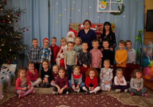 Mikołaj, panie nauczycielki i dzieci zgrupy III pozują do zdjęcia na tle świątecznej dekoracji