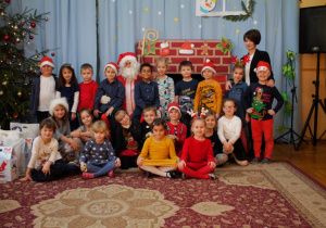 Mikołaj, dzieci z najstarszej grupy przedszkolnej ze swoją panią pozują do zdjęcia na tle niebieskiej dekoracji