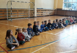 dzieci siedzą w równym szeregu na podłodze, w tle widać bramkę