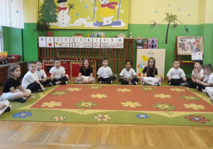 dzieci ubrane w stroje biało - czarne siedzą na dywanie w siadzie skrzyżnym