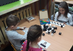 dzieci siedzą przy stoliku, układają klocki biało - czarne według wzoru
