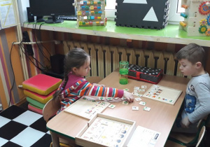 dzieci siedza przy stoliku, układają drewniane puzzle