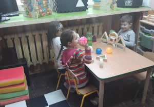 zadowolone dzieci siedza przy stoliku, bawią się kolorowymi piłeczkami i klockami
