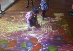 dziewczynka kuca, zabawa na dywanie interaktywnym
