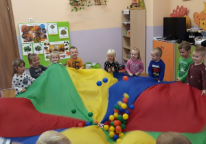 dzieci podrzucają kolorowe piłeczki ułożone na chuście