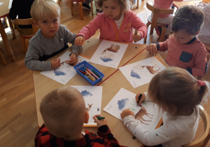 dzieci siedza przy stoliku, rysują trawkę