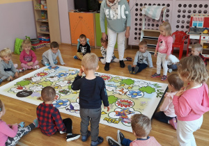 dzieci siedzą wokół dużej gry planszowej rozłożonej na podłodze