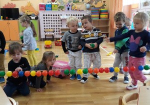 dzieci bawią sią kolorowymi piłeczkami, przyklejają do taśmy