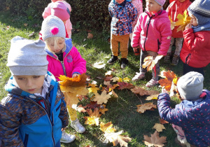 dzieci układają obrazek z liści na trawie