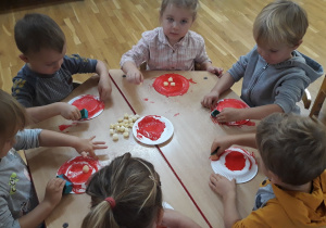 przedszkolaki ozdabiają czerwoną farbą kapelusz muchomora