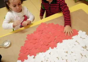 dzieci wyklejają serce biało czerwonymi kwiatami