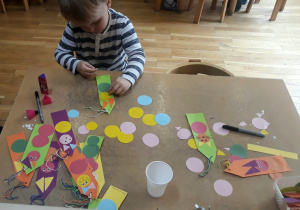 chłopiec nakleja figury geometryczne na kolorowa kartkę papieru