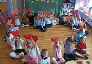 dzieci siedza w dłoniach trzymają czerwone serduszka