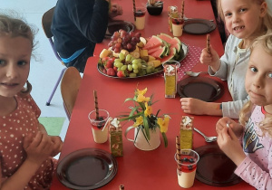 dzieci siedzą przy stole na którym ustawione są smakołyki