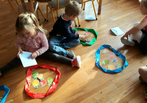 dzieci siedzą na podłodze przed nimi leżą szarfy, przedszkolaki tworzą zbiory owoców