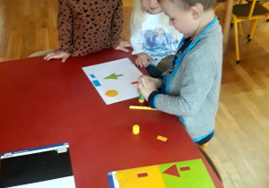 dzieci wykonują pracę plastyczną z kolorowych figur geometrycznych