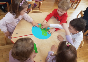 dzieci siedza przy stolikach, malują farbami
