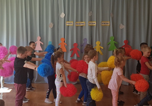 dzieci tańczą z kolorowymi pomponami zwrócone w prawą stronę