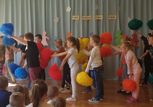 dzieci tańczą z kolorowymi pomponami zwrócone w lewą stronę