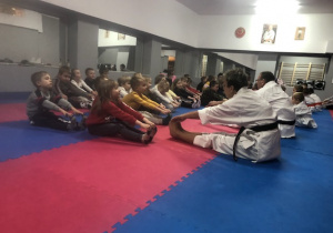 dzieci siedzą na niebiesko różowych matach, wykonują ćwiczenia z instruktorami karate