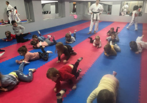 dzieci ćwiczą na niebiesko różowych matach, wykonują ćwiczenia z instruktorami karate