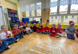 dzieci siedzą na podłodze w czerwonych czapkach
