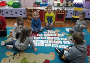 dzieci siedzą na dywanie, przed dziećmi rozłożone są koperty w kształcie prezentu