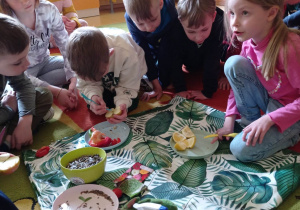 dzieci wyjmują nasionka z owoców: jabłek, pomarańczy