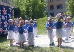 dzieci z najmłodszej grupy ubrane w stroje niebiesko-białe trzymają się za ręce i obracają się wkoło