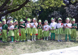 dzieci z grupy II ubrane w stroje zielono białe na głowach opaski z wizerunkiem żaby trzymają w dłoniach instrumenty