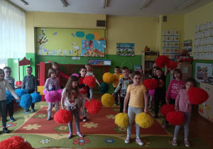 przedszkolaki tańczą z kolorowymi pomponami w sali przedszkolnej
