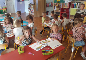 przedszkolaki podczas zajęć, siedzą przy stolikach i wykonuja zadania w kartach pracy