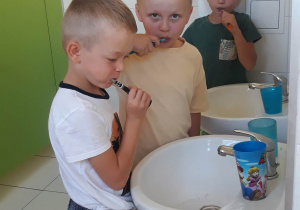 chłopcy myją zęby, stoją przed umywalką