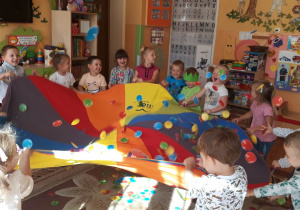 dzieci trzymają w dłoniach dużą kolorową chustę i podrzucają kolorowe kropki