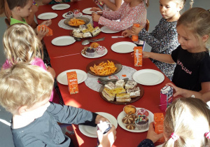 przedszkolaki siedzą przy stole na którym leży słodki poczęstunek