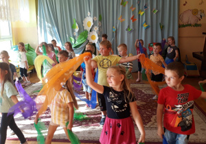 dzieci ustawione w rzędzie, trzymają w dłoniach kolorowe chusty, tańczą do wesołej muzyki