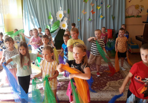 dzieci ustawione w rzędzie, trzymają w dłoniach kolorowe chusty, tańczą do wesołej muzyki