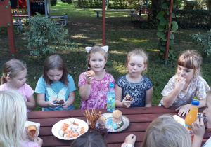 dzieci w ogrodzie przedszkolnym siedzą przy stole i jedzą babeczki