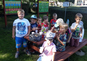 w ogrodzie przedszkolnym dzieci siedzą przy stołach i jedzą babeczki