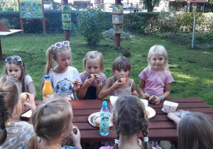 dziewczynki siedzą w ogrodzie przedszkolnym i spożywają słodki poczęstunek