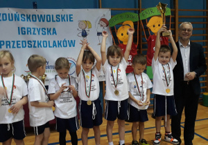 dzieci stoją na podium z medalami i pucharem