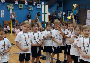 dzieci w strojach sportowych pozują do zdjęcia, chłopiec w dłoni trzyma puchar, nagroda za udział w zawodach