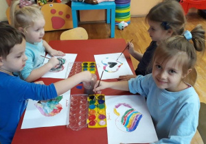 dzieci siedza przy stolikach, malują farbami serce