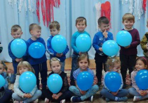 dzieci ubrane na niebiesko, trzymają w dłoniach niebieskie baloniki