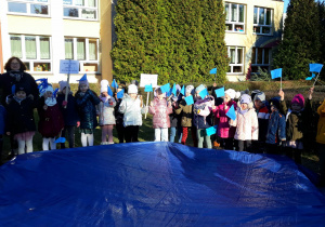 dzieci stoją z transparentami na tle niebieskiej ziemi