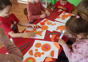 dzieci wyklejają misia z pomarańczowych kół