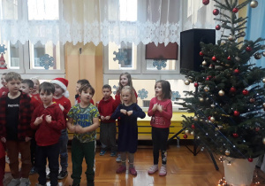 dzieci śpiewają stojąc przy choince