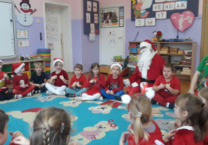 dzieci siedzą na dywanie z Mikołajem i Elfem, śpiewają piosenkę