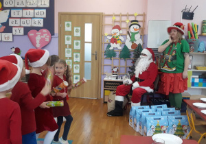 dzieci tańczą dla Mikołaja, który obserwuje występ razem z Elfem